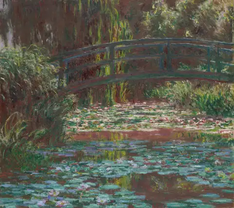 A green footbridge over a pond covered in water lilies, framed by willows and reeds.